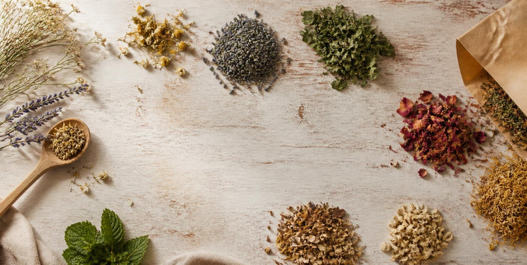 Herbes et fleurs séchées en vrac disposées sur une table de bois clair, avec une cuillère de bois et un sachet kraft
